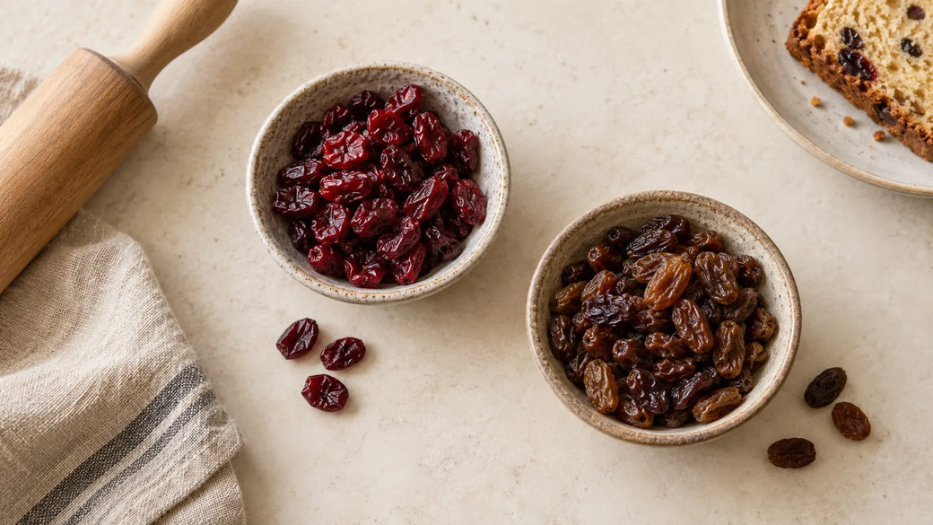 Getrocknete Cranberrys und Rosinen in getrennten Schälchen neben einfachem Gebäck.