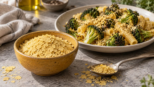 Goldene Hefeflocken in einer Schale und auf einem Löffel neben Pasta mit geröstetem Brokkoli.