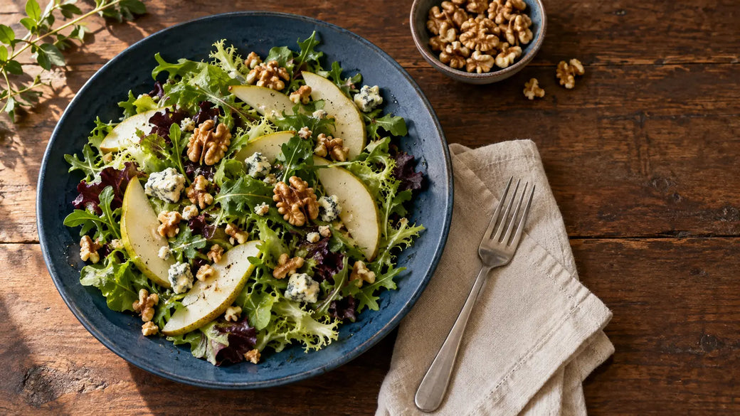 Blattsalat mit Birnenscheiben, Walnussstücken und Blauschimmelkäse auf einem blauen Teller.
